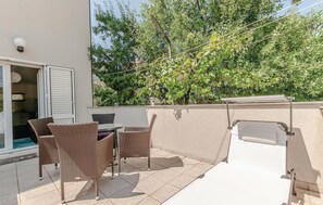 Une terrasse extérieure aménagée avec des meubles en osier, un barbecue et une vue sur des arbres et un bâtiment.