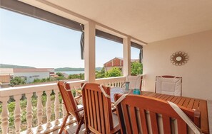 A balcony with a wooden table and chairs, a view of buildings and hills, and a decorative wall piece. - 2 bedroom beach front apartment in Pirovac (Pirovac)