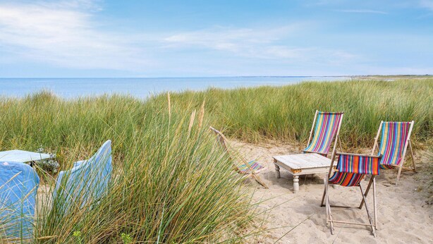 Une plage avec deux chaises de plage à rayures et une petite table, le tout entouré d’herbes hautes.