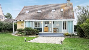 Une maison à deux étages, avec un toit en tuiles, un porche à l’avant et un petit jardin.