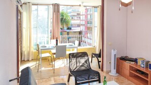A living room with a sofa, a dining table with chairs, a balcony with a view of buildings, and a standing heater. - Cozy apartment in Alicante with WiFi (Alicante)