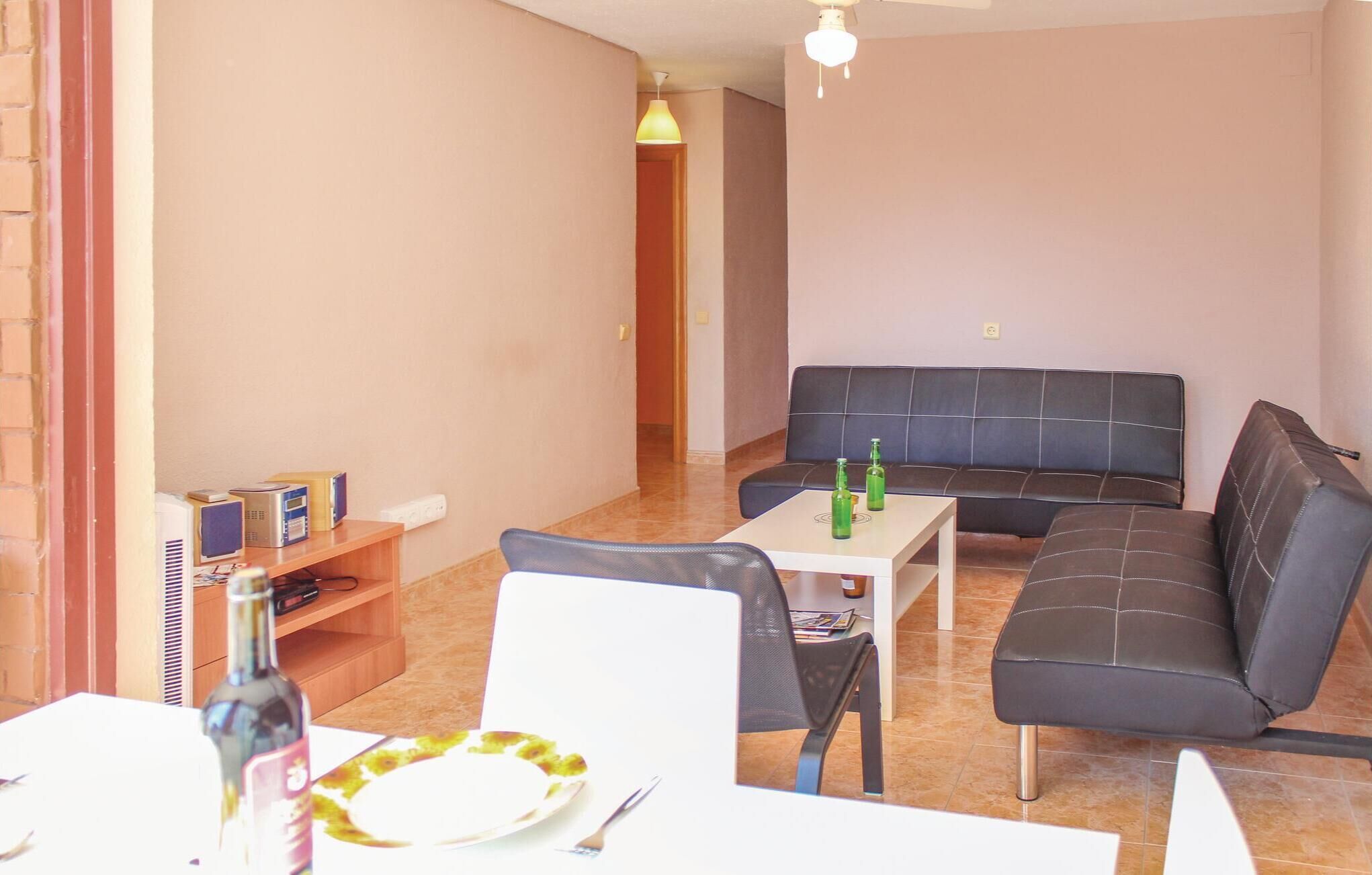 Una sala de estar con un sofá, una mesa de comedor y un televisor. Hay una botella sobre la mesa.