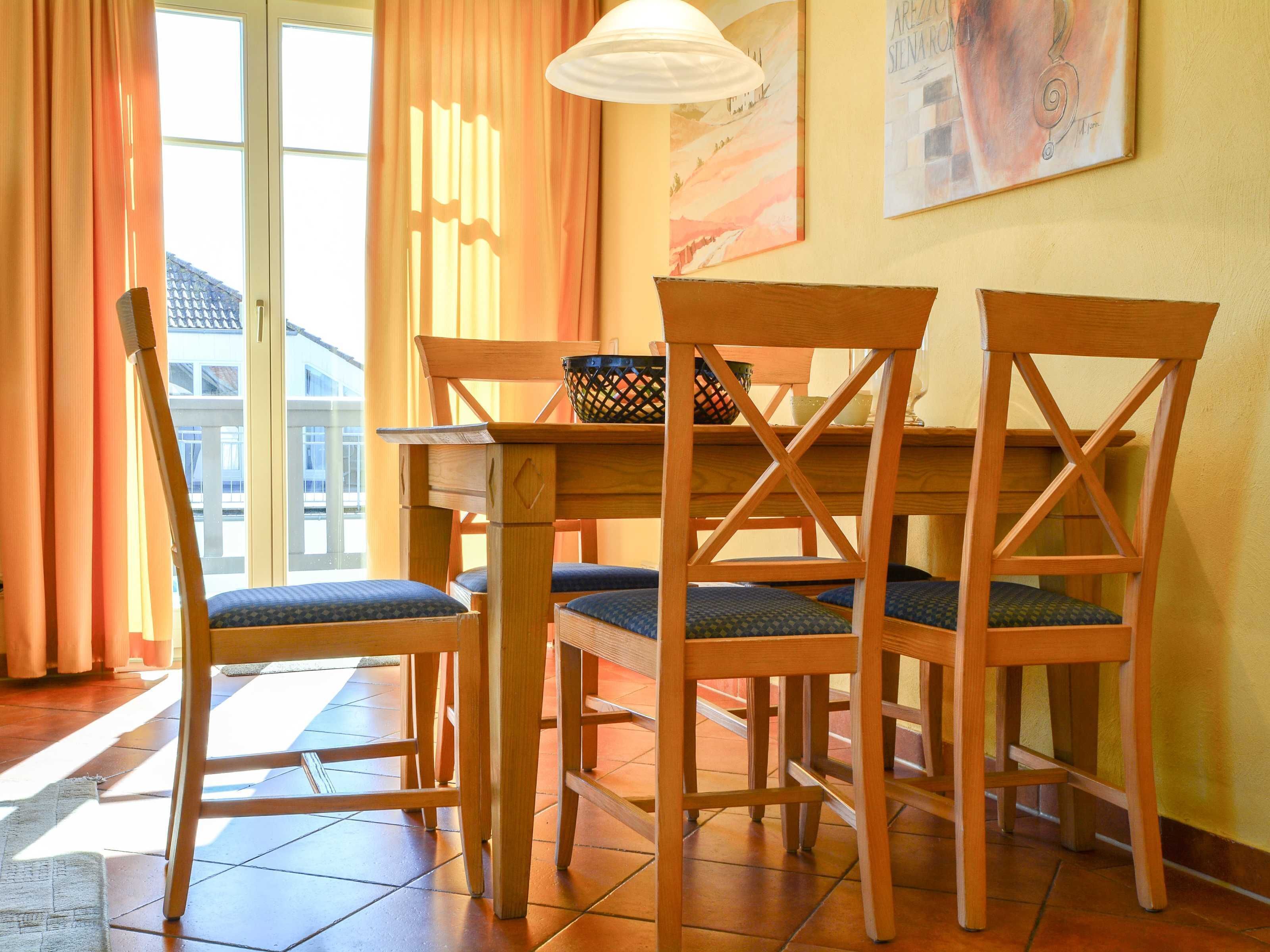 A dining area with a wooden table and four chairs, a basket on the table, and a painting on the wall.