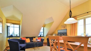 Una sala de estar acogedora con un sofá, sillas, una mesa de comedor y un televisor.