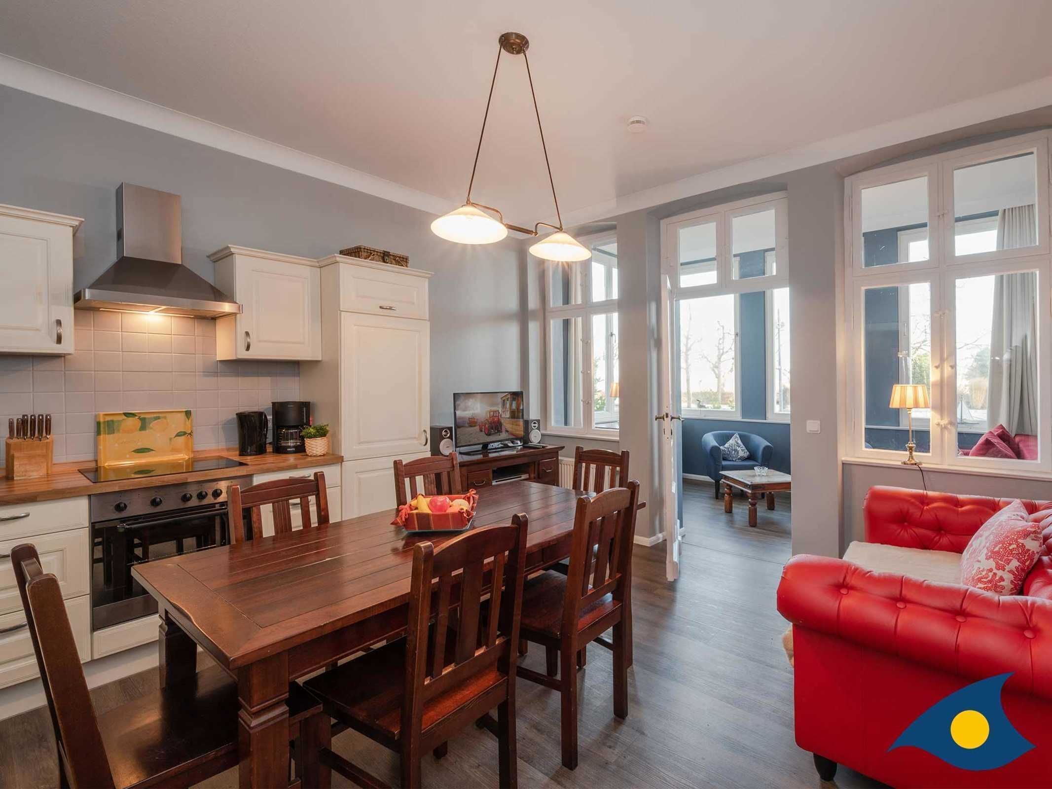A modern kitchen with white cabinets, a wooden dining table, and a red sofa.