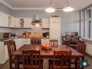 Una cocina moderna con armarios blancos, una mesa de comedor con sillas, un microondas, una estufa y un televisor.