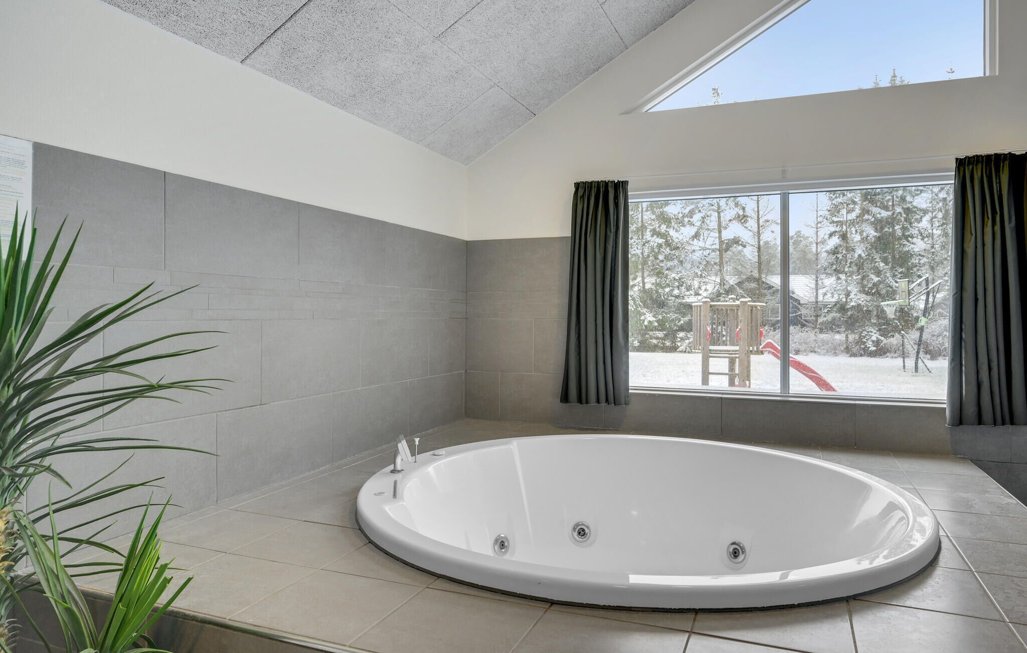 A modern bathroom with a freestanding bathtub, large windows, and a view of a snowy landscape.