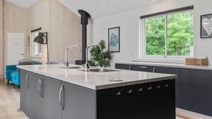 Een moderne keuken met een groot eiland, roestvrijstalen apparatuur en uitzicht op groen.