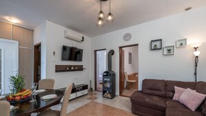 A modern living room with a brown sofa, a dining area with a table and chairs, a TV mounted on the wall, and a fireplace. - 2 bedroom nice apartment in Krnica (Krnica)