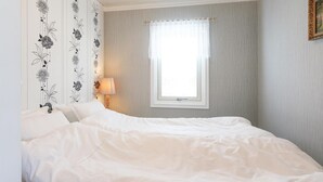 A neatly made bed in a room with a window, a lamp, and floral wallpaper. - 2 bedroom awesome home in Sölvesborg (Sölvesborg)