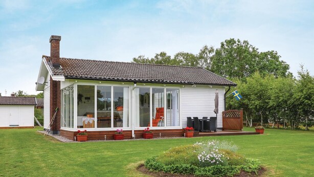A single-story house with a tiled roof, large glass windows, and a small porch with outdoor seating. - 2 bedroom awesome home in Sölvesborg (Sölvesborg)