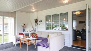 A cozy living room with a white sofa, a wooden coffee table, and a fireplace. There are large windows with lace curtains, and a door leading to another room. - 2 bedroom awesome home in Sölvesborg (Sölvesborg)
