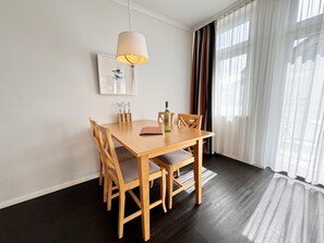 Un comedor con una mesa y sillas de madera, una lámpara colgante, un cuadro enmarcado y una botella sobre la mesa.
