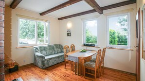 A cozy room with a wooden floor, a sofa, a dining table with chairs, and large windows offering a view of greenery outside. - Beautiful home in Wicko with WiFi (Wicko)