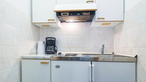 A compact kitchen with a built-in refrigerator, a coffee maker, and a stainless steel sink.