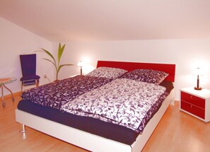A bedroom with a bed, two bedside tables, a chair, and a potted plant.