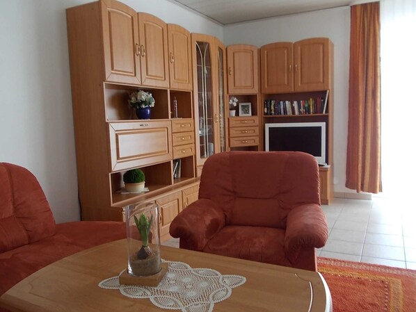 Un salon comprenant un canapé, une table basse avec une plante, des meubles en bois, un téléviseur et une bibliothèque.