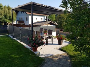 A covered patio with a table and chairs, surrounded by a fence and potted plants.