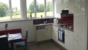 A kitchen with a dining area, large windows, and a dishwasher. - Apartment Schafberg - Gästehaus Wienerroither (Mondsee)