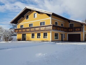 A two-story building with a garage, a balcony with decorative trim, and a snow-covered ground.