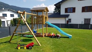A playground with a slide and climbing structures, surrounded by a fenced area with a grassy lawn. - Apartment Schafberg - Gästehaus Wienerroither (Mondsee)
