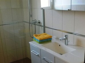 A bathroom with a white sink, a mirror, and a shower. There are towels stacked on the sink.