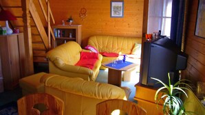 Un salon chaleureux avec un canapé jaune, une petite table, un téléviseur et un escalier menant à un autre niveau.