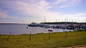 Un port de plaisance où sont amarrés différents types de bateaux, une zone herbeuse au premier plan et une étendue d’eau en arrière-plan.