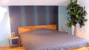 A wooden bed with a blue headboard and a grey bedspread in a room with wooden flooring and a blue accent wall.