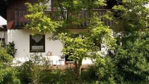 A two-story building with a balcony, surrounded by lush greenery.