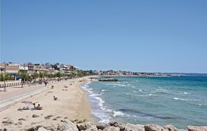 A beach with a promenade, rocky shoreline, and buildings in the background.