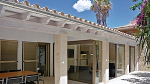 A covered outdoor area with a table and chairs, large glass doors leading to a room, and a palm tree in the background. - 4 bedroom awesome home in Palma de Mallorca (Palma de Mallorca)