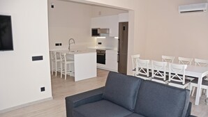 A modern living room with a grey sofa, a dining area with white chairs, a kitchen with white cabinets and stainless steel appliances, and a flat-screen TV mounted on the wall. - 4 bedroom awesome home in Palma de Mallorca (Palma de Mallorca)