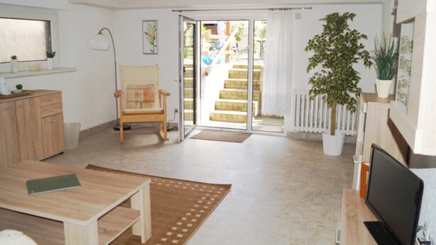 A bright living room with a wooden table, a chair, a TV, and a potted plant. - Apartment Starfish - Apartment starfish (Graal-Müritz)
