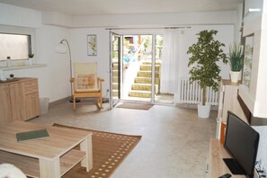 A bright living room with a wooden table, a chair, a TV, and a potted plant.