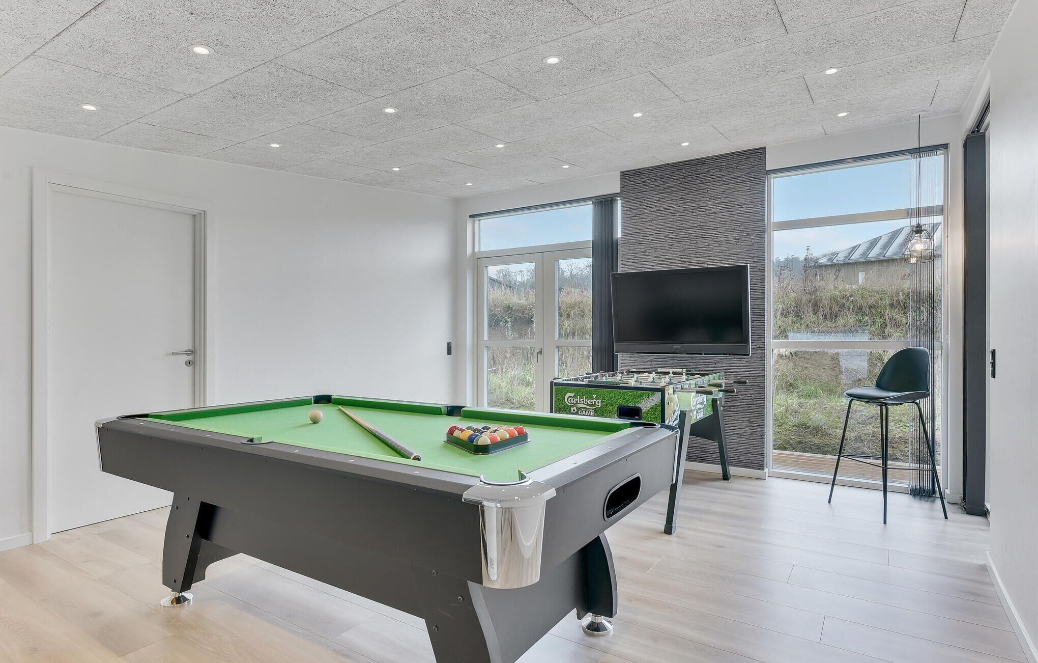 Un espace de loisirs intérieur moderne, équipé d’une table de billard, d’un baby-foot et d’un grand écran de télévision.