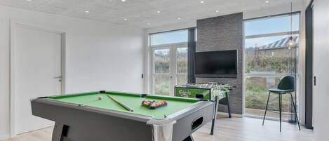 Un espace de loisirs intérieur moderne, équipé d’une table de billard, d’un baby-foot et d’un grand écran de télévision.