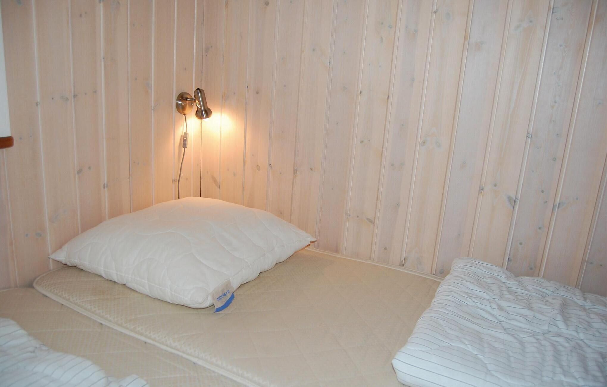 Ein Einzelbett mit weißer Matratze und Kissen, eine Wandleuchte und eine Wandverkleidung aus Holz.