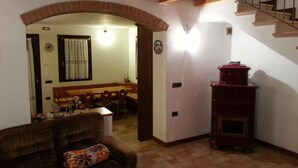 A cozy living room with a fireplace, a dining area with a wooden table and chairs, and a staircase. - Holiday home with garden and mountain view (Velo d Astico)