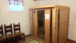 A room with a wooden cabinet, three wooden chairs, a green rug, and a window with checkered curtains. - Holiday home with garden and mountain view (Velo d Astico)