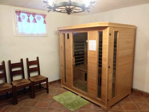 A room with a wooden cabinet, three wooden chairs, a green rug, and a window with checkered curtains.
