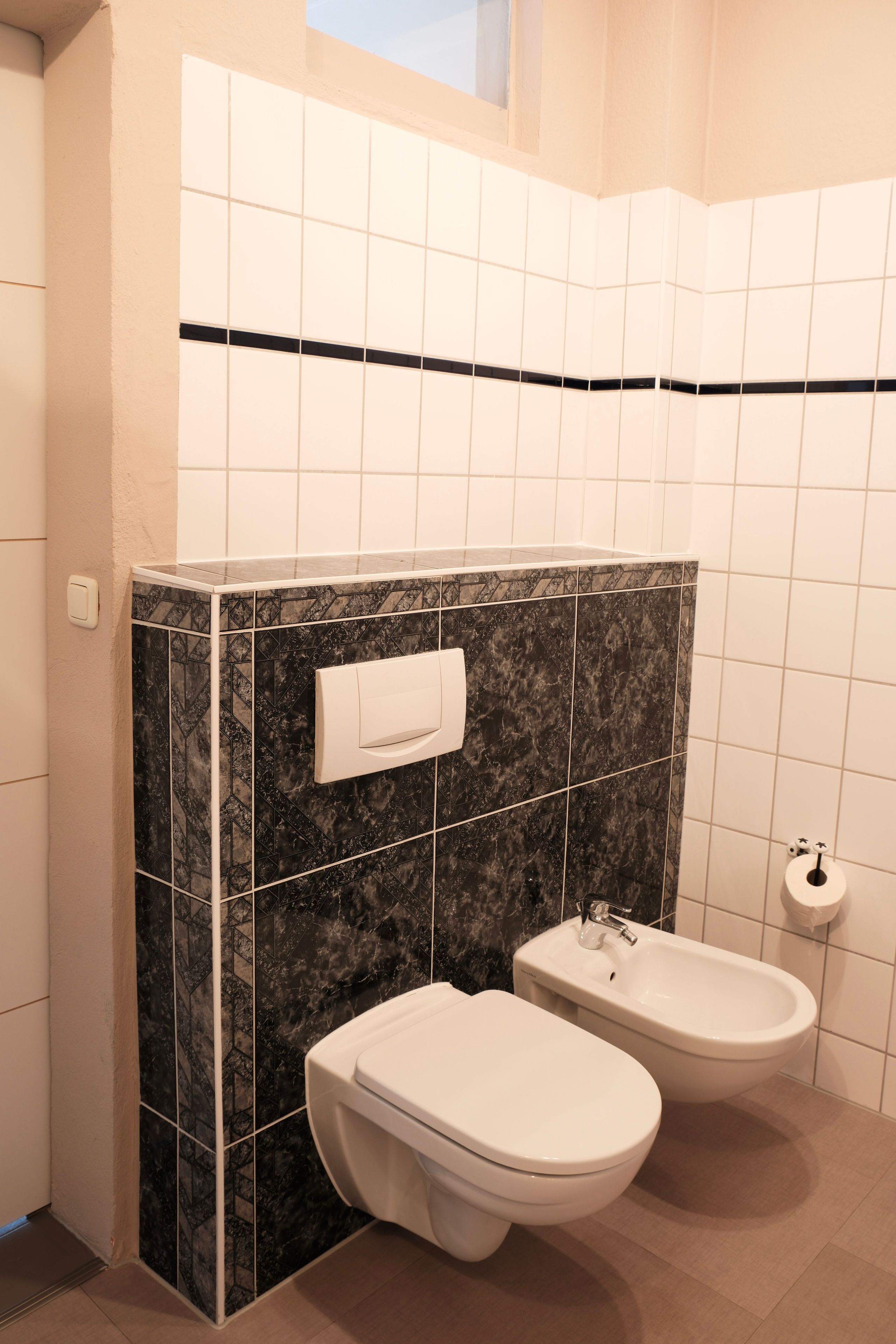 Een badkamer met toilet, bidet en een handdoekhouder aan een betegelde muur.
