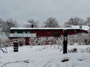 A red building with a balcony, surrounded by snow-covered vegetation.