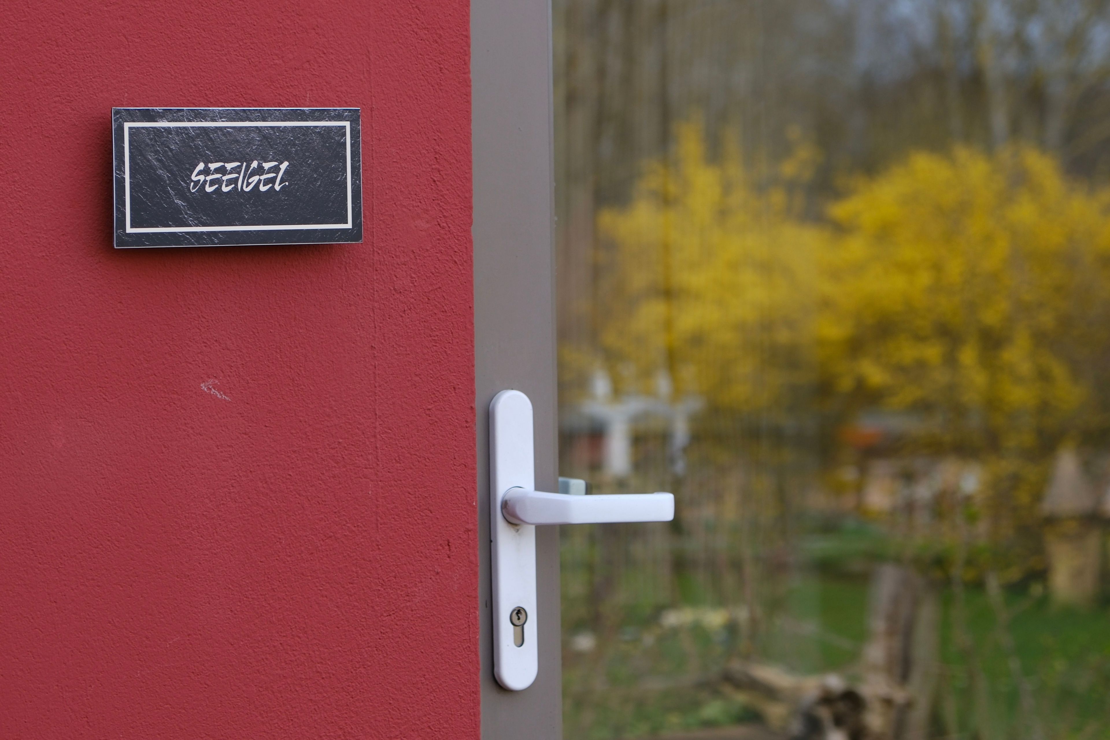 A door with a white handle and a keyhole, a black sign with white text, and a blurred background with yellow foliage.