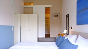 Una camera da letto con un letto, cuscini, un armadio, uno specchio e un quadro appeso al muro.