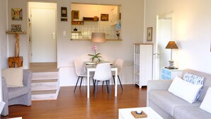 Un soggiorno moderno con zona pranzo, una scala e una cucina visibile attraverso un'apertura.