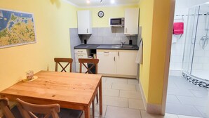 Eine kleine Küche mit weißen Schränken, einer Mikrowelle und einem Spülbecken. Ein Holztisch mit Stühlen und eine Karte an der Wand.