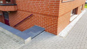 Ein Backsteinhaus mit roter Tür, lilafarbenem Geländer und einem blauen Fliesenstufen.