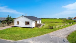 Een wit huis met één verdieping, een omheinde tuin en een oprit met grind.