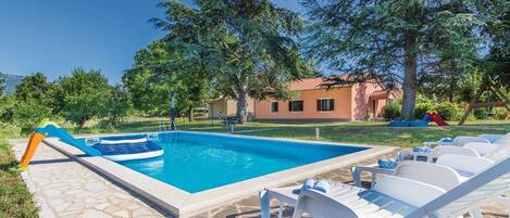 A swimming pool with lounge chairs and a slide, surrounded by trees and a house.